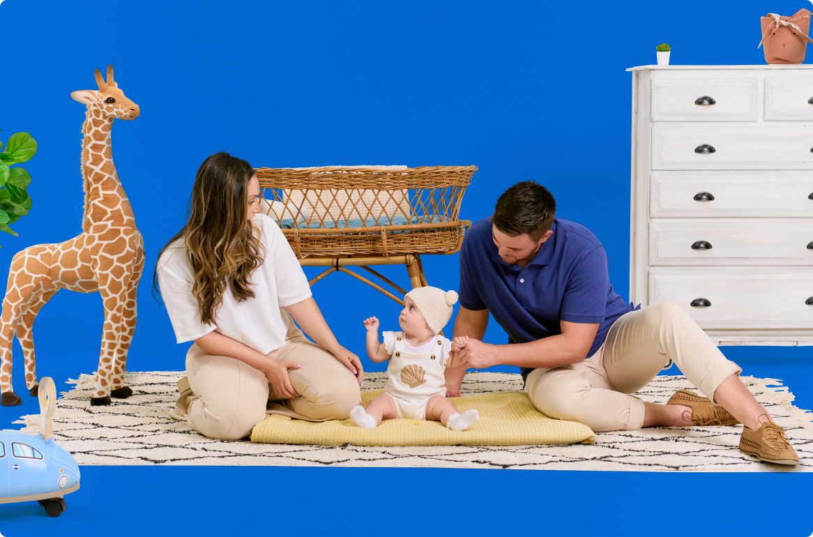 A family is sitting on a rug with a baby and a giraffe.