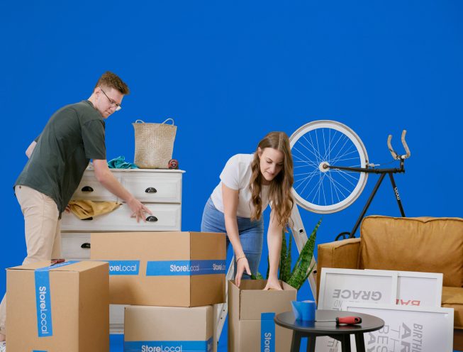 A man and woman moving boxes on a blue background.